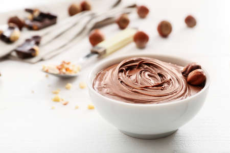 Bowl with tasty chocolate paste and hazelnuts on white wooden backgroundの写真素材