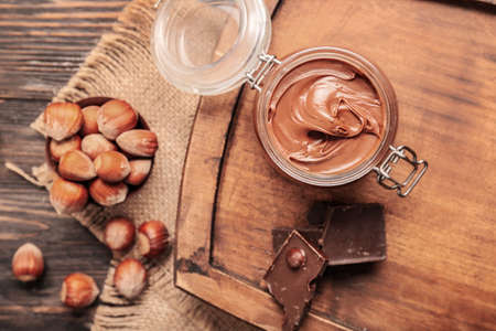 Jar with tasty chocolate paste and hazelnuts on tableの写真素材
