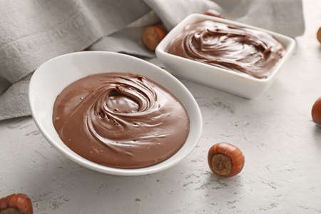 Bowls with tasty chocolate paste and hazelnuts on light backgroundの写真素材