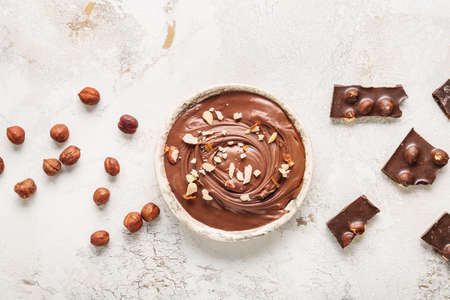 Bowl with tasty chocolate paste and hazelnuts on light backgroundの写真素材
