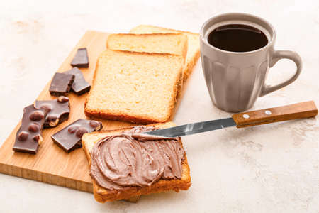 Fresh bread with chocolate paste and cup of coffee on light backgroundの写真素材