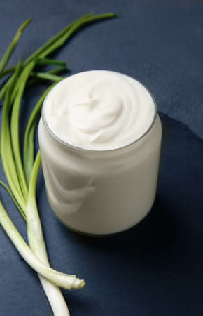 Jar of tasty sour cream and green onion on dark tableの写真素材