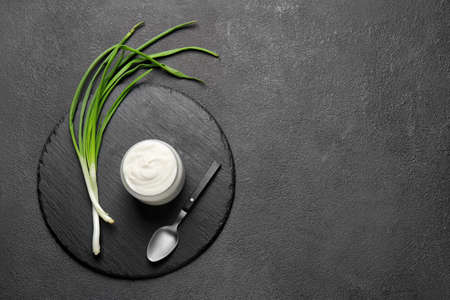 Jar of tasty sour cream and green onion on dark tableの写真素材
