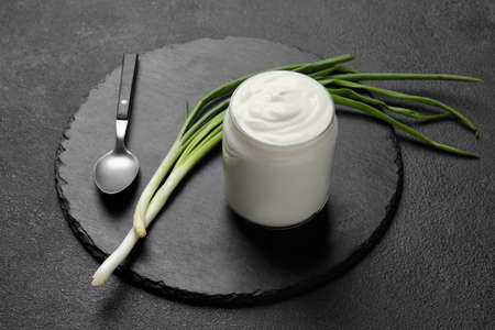 Jar of tasty sour cream and green onion on dark tableの写真素材
