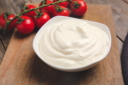 Bowl of tasty sour cream and tomatoes on wooden tableの写真素材