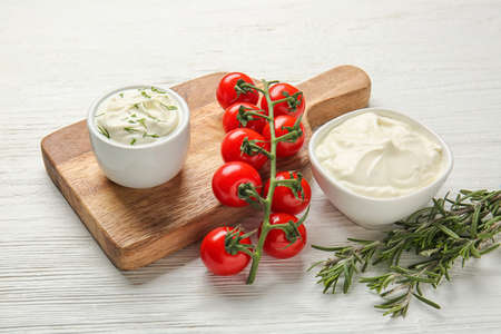 Tasty sour cream and tomatoes on white wooden table