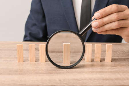 Man looking at wooden blocks on table through magnifier. Concept of dismissalの写真素材