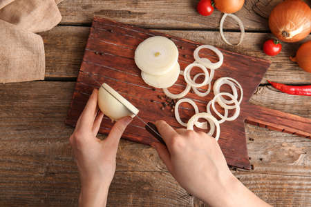 Woman cutting fresh raw onion on wooden tableの写真素材