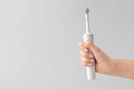 Female hand with electric tooth brush on light backgroundの写真素材