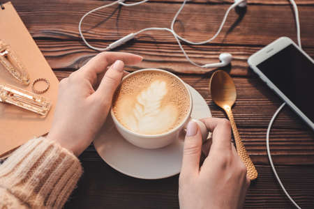Woman drinking tasty cappuccino at wooden tableの写真素材