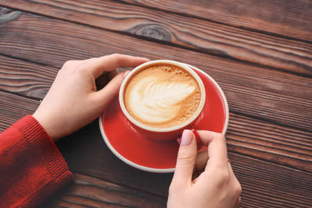 Woman drinking tasty cappuccino at wooden tableの写真素材