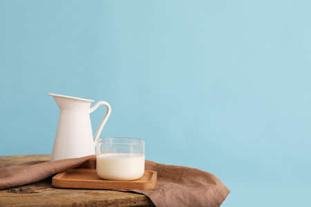 Glass and jug of fresh milk on table against color backgroundの写真素材