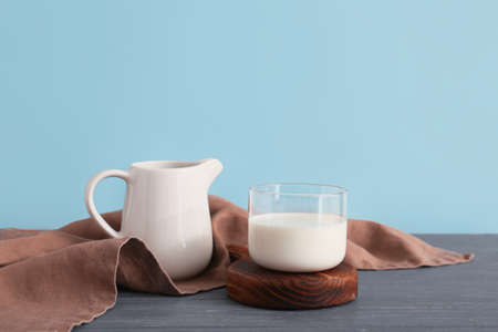 Glass and jug of fresh milk on table against color backgroundの写真素材