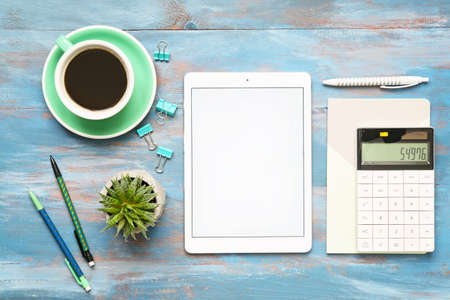 Tablet computer, calculator, cup of coffee and stationery on wooden background