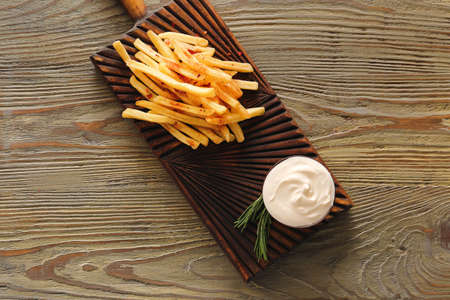 Board with tasty sour cream and french fries on tableの写真素材
