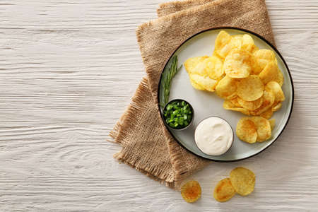 Plate with tasty sour cream, green onion and potato chips on tableの写真素材