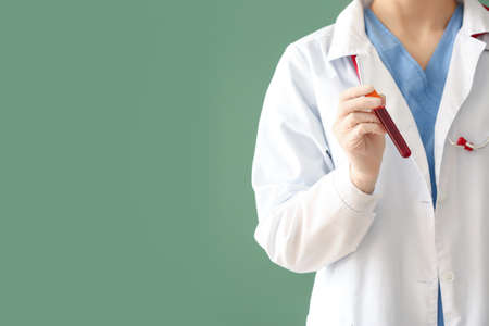 Doctor holding test tube with blood sample on color backgroundの写真素材