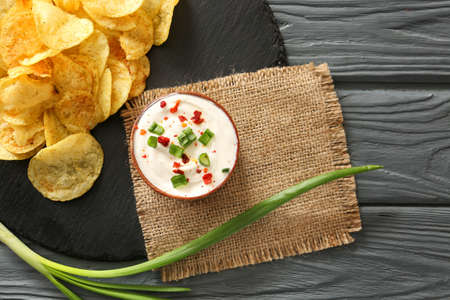 Bowl with tasty sour cream, green onion and potato chips on tableの写真素材