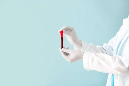 Doctor holding test tube with blood sample on color backgroundの写真素材