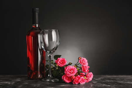 Bottle of wine, glass and roses on table against dark backgroundの写真素材