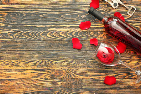 Bottle of wine, glass, rose and petals on wooden tableの写真素材