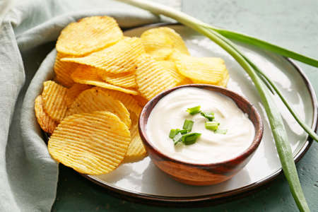 Tasty sour cream, green onion and potato chips on tableの写真素材