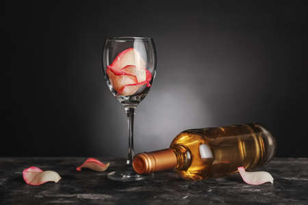 Bottle of wine and glass with rose petals on table against dark backgroundの写真素材