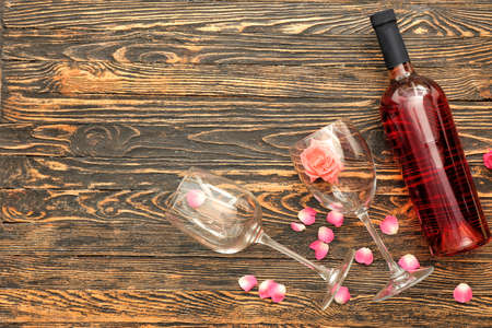 Bottle of wine, glasses and rose petals on wooden tableの写真素材