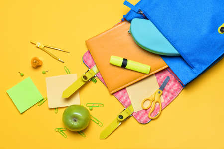School backpack and stationery on color background