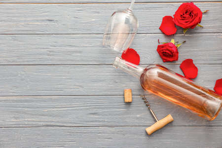 Glass with bottle of wine, corkscrew and rose flowers on wooden backgroundの写真素材