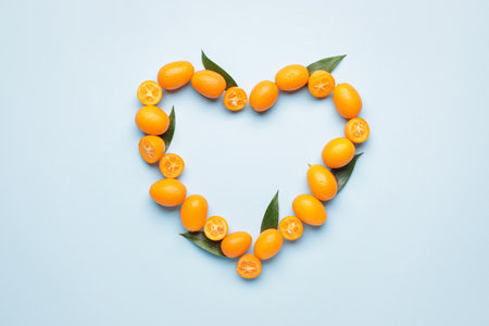 Heart made of tasty kumquat fruit on color backgroundの写真素材