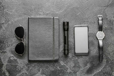 Modern flashlight with mobile phone, notebook, sunglasses and clock on dark backgroundの写真素材