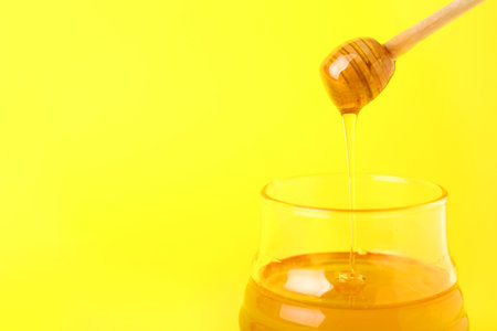 Honey dripping from dipper into jar on color backgroundの写真素材