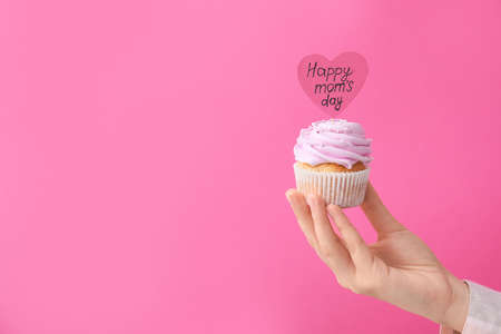 Female hand with tasty cupcake for Mother's Day on color backgroundの写真素材