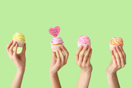 Female hands with tasty cupcakes for Mother's Day on color backgroundの写真素材
