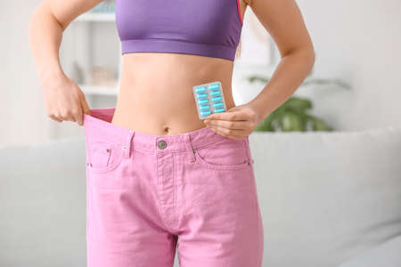 Woman in loose clothes and with weight loss pills at homeの写真素材