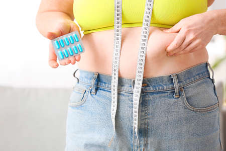 Woman with weight loss pills and measuring tape at home, closeup