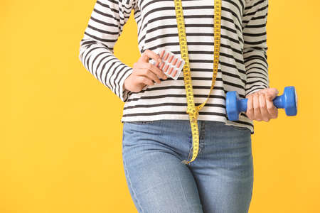 Woman with weight loss pills, measuring tape and dumbbells on color backgroundの写真素材