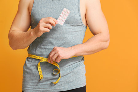 Young man with weight loss pills and measuring tape on color backgroundの写真素材