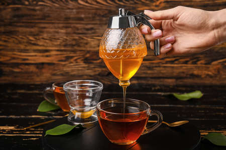 Female hand pouring tasty honey from jar into cup on tableの写真素材