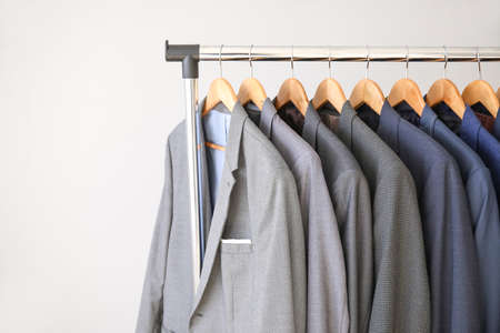 Hanger with different stylish male suits on light backgroundの写真素材