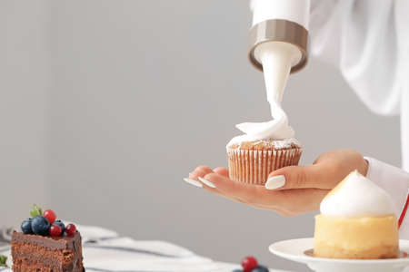 Female confectioner cooking tasty dessert on gray backgroundの写真素材