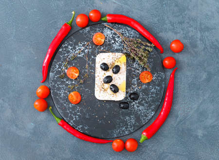 Board with tasty feta cheese, vegetables and spices on dark backgroundの写真素材