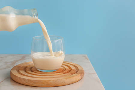 Pouring of milk into glass on table against color backgroundの写真素材