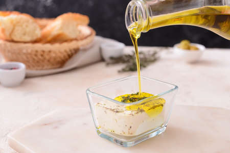 Pouring of olive oil onto tasty feta cheese in bowl on tableの写真素材