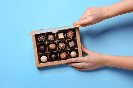 Female hands holding box with delicious chocolate candies on color backgroundの写真素材
