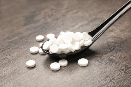 Spoon with pills on wooden background