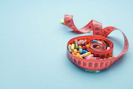 Measuring tape and weight loss pills on color backgroundの写真素材