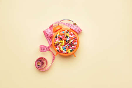 Measuring tape, alarm clock and weight loss pills on color backgroundの写真素材