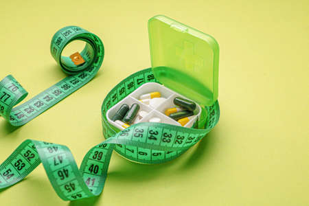 Box with weight loss pills and measuring tape on color backgroundの写真素材